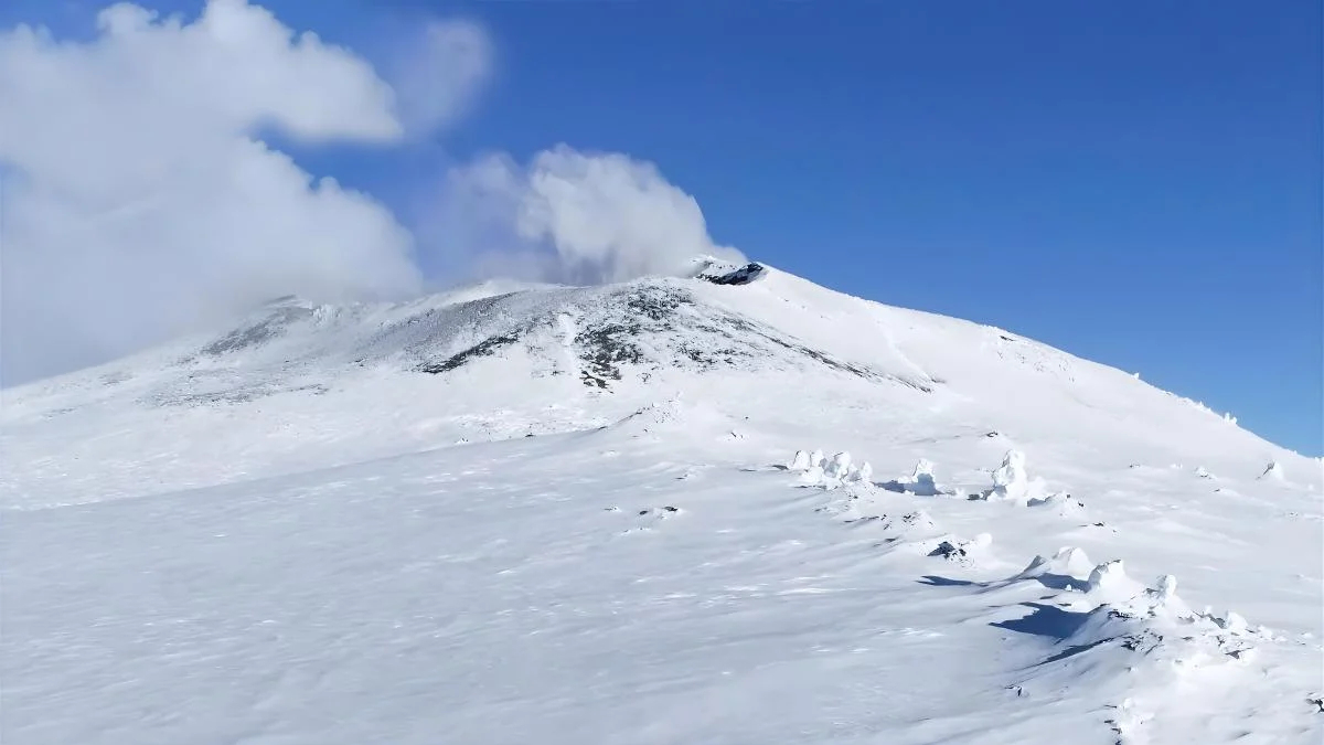 Snow-covered mountain slope under a blue sky with a few clouds.