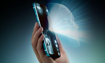Hand holding a teal smartphone with a glowing brain hologram projecting from the screen, symbolizing AI technology