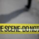 Yellow crime scene tape reading 'CRIME SCENE- DO NOT ENTER' stretched across a blurred outdoor area, signaling a restricted area.