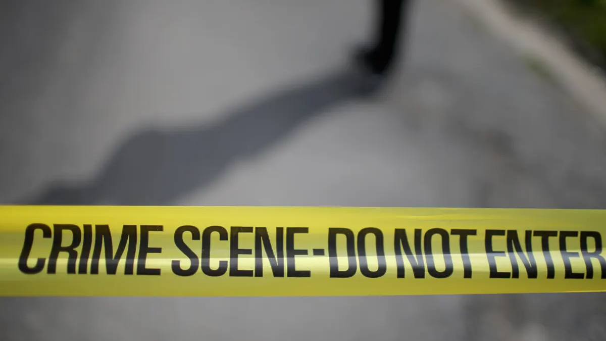 Yellow crime scene tape reading 'CRIME SCENE- DO NOT ENTER' stretched across a blurred outdoor area, signaling a restricted area.