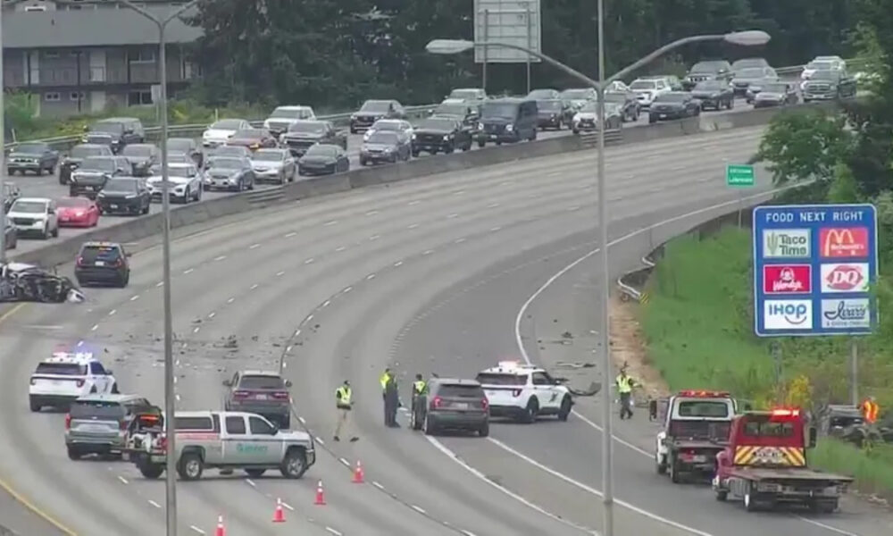 Multi-vehicle collision on a divided highway with emergency responders directing traffic and cones on the roadway far from a green exit sign panel on the right side of the scene.
