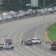 Multi-vehicle collision on a divided highway with emergency responders directing traffic and cones on the roadway far from a green exit sign panel on the right side of the scene.