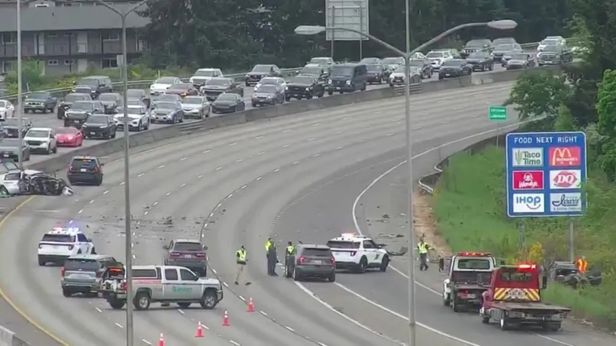 Multi-vehicle collision on a divided highway with emergency responders directing traffic and cones on the roadway far from a green exit sign panel on the right side of the scene.