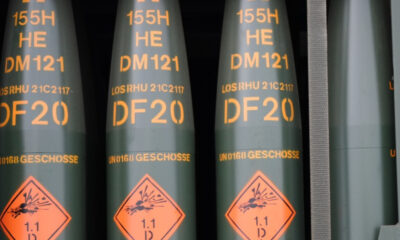 Row of green cylindrical ordnance with orange DF20 markings and a diamond warning label showing explosive hazard (1.1).