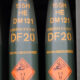 Row of green cylindrical ordnance with orange DF20 markings and a diamond warning label showing explosive hazard (1.1).