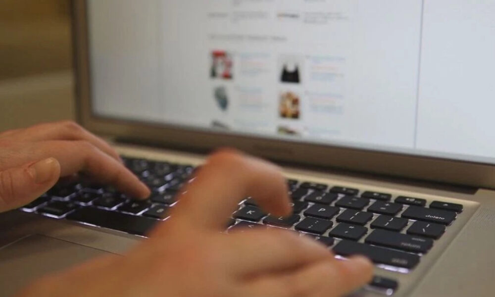Hands typing on a laptop keyboard with a blurred webpage visible on the screen