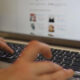 Hands typing on a laptop keyboard with a blurred webpage visible on the screen