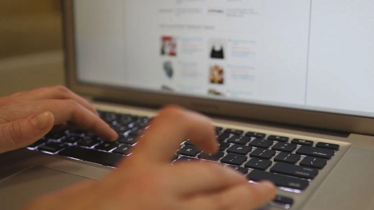 Hands typing on a laptop keyboard with a blurred webpage visible on the screen