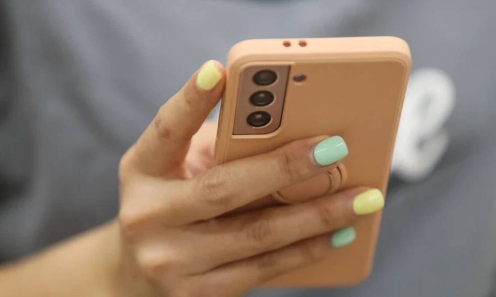 Close-up of a hand with pastel nails holding a rose-gold smartphone with a triple-camera setup.