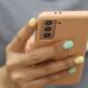 Close-up of a hand with pastel nails holding a rose-gold smartphone with a triple-camera setup.