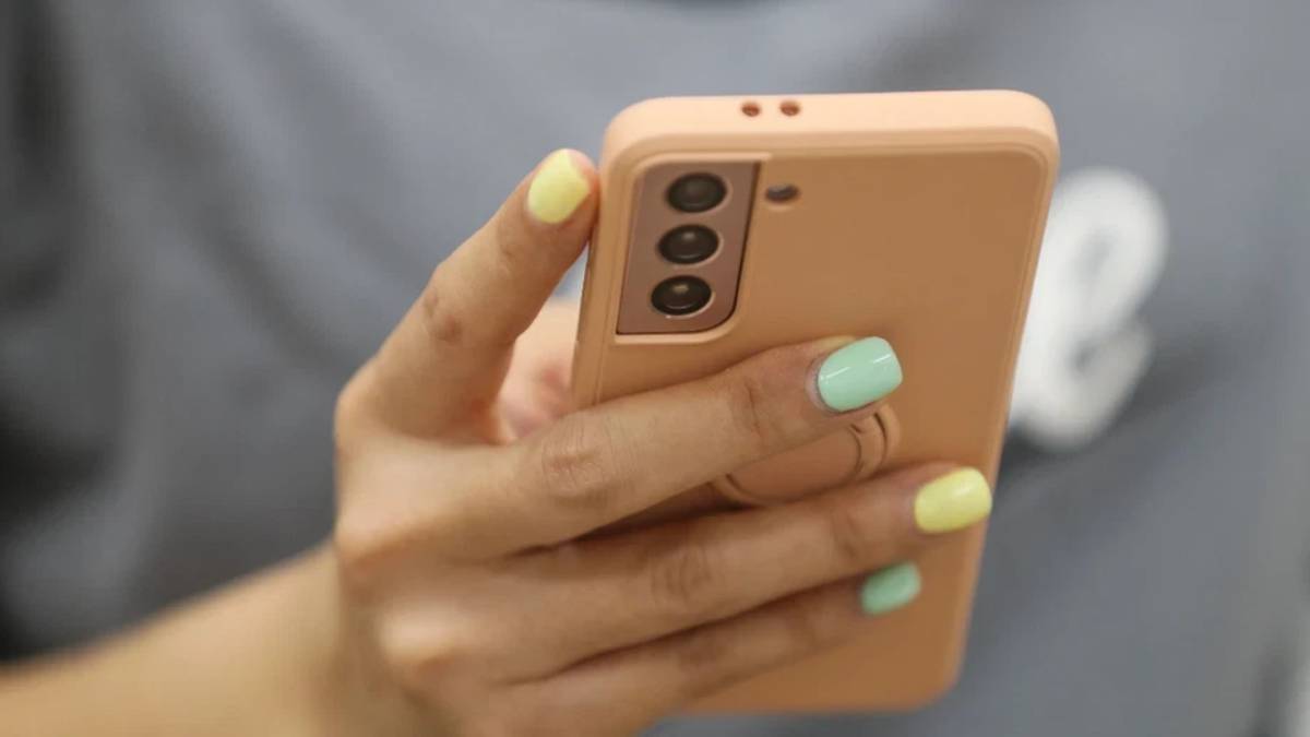 Close-up of a hand with pastel nails holding a rose-gold smartphone with a triple-camera setup.