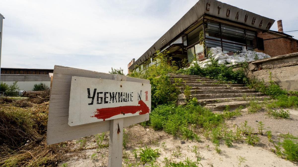 Abandoned building with overgrown vegetation and a weathered sign in Russian pointing right toward shelter 1.