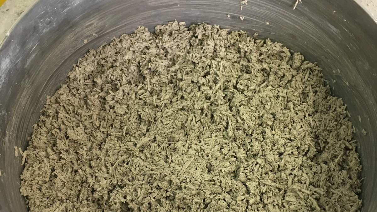 Greenish-gray shredded material filling a large round metal tub, like wood chips or fiber shreds.
