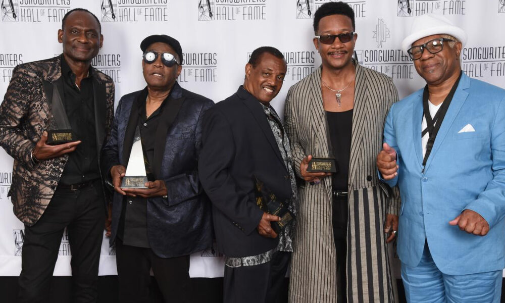 Five men pose on a red carpet backdrop reading Songwriters Hall of Fame, each holding a trophy award.