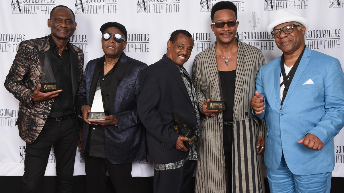 Five men pose on a red carpet backdrop reading Songwriters Hall of Fame, each holding a trophy award.