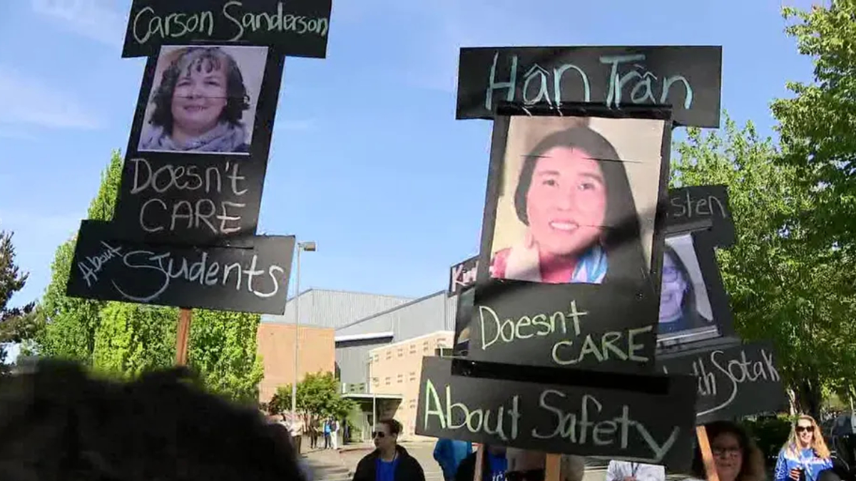 Protesters hold black signs with chalky white text and portrait photos; messages say 'Doesn't CARE About Students' and similar statements.