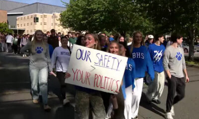 Group of students marching outside, holding a sign that reads "Our Safety > Your Politics" during a campus demonstration.
