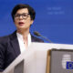 Woman in a dark blazer delivers a speech at a podium with the EU emblem against a blue backdrop.