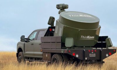 Pickup truck with a large ThinkKom industrial unit mounted on a flatbed, standing in a grassy field.