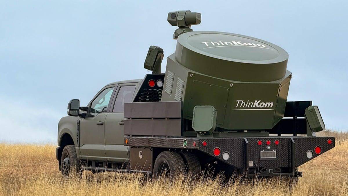 Pickup truck with a large ThinkKom industrial unit mounted on a flatbed, standing in a grassy field.