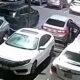 White sedan with open driver's door in a crowded parking lot; a person stands near it on the right side of the image.