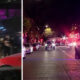 Nighttime street scene with police cars and flashing lights on a busy avenue; a split-screen shows people running on a sidewalk in the left frame, caption reads 'Another shooting'
