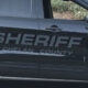 Black sheriff SUV side with large 'SHERIFF CHELAN COUNTY' lettering and a circular sheriff badge on the front door