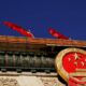 Close-up of China's national emblem mounted on a building, with red flags fluttering against a deep blue sky.