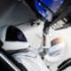 Astronaut in white suit and helmet reaches for cockpit controls inside a spacecraft, Earth visible through a circular window behind.