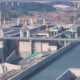 Large-scale bridge construction over a canal with yellow cranes, concrete supports, and unfinished roadway sections; waterway on both sides surrounded by concrete barriers