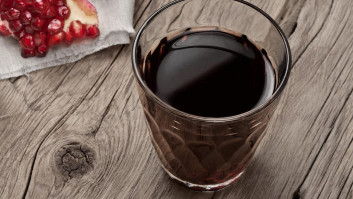 Glass of red wine on a weathered wooden table with pomegranate seeds on a white napkin in the corner on the left.