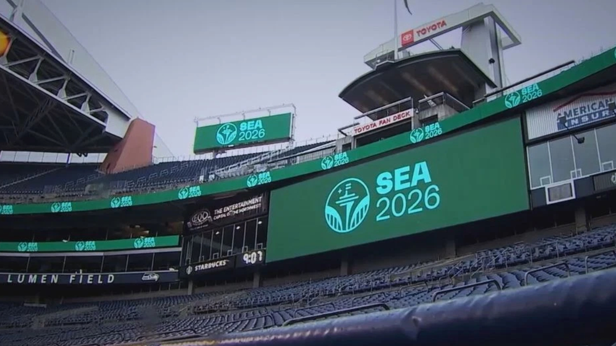 Stadium concourse with a large LED screen reading SEA 2026 and a teal logo, with Lumen Field signage visible in the stands.