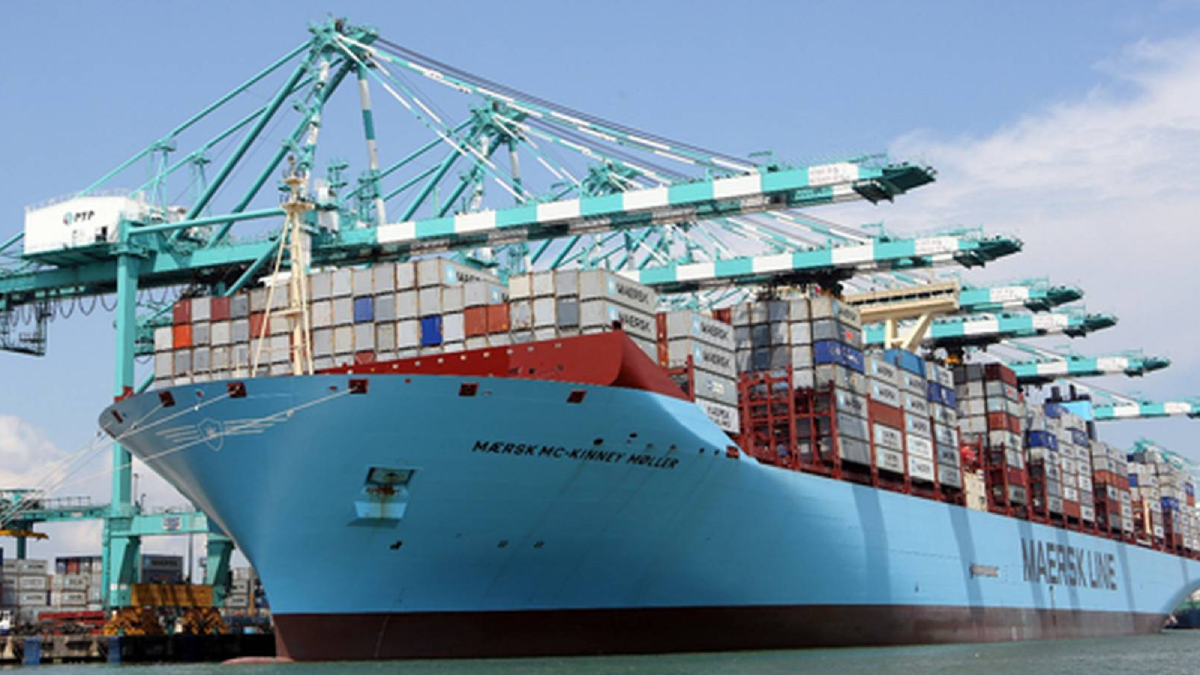 Blue Maersk container ship at a port with stacked cargo containers and teal gantry cranes overhead.