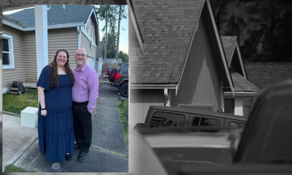 Smiling couple standing together in a driveway outside a beige house; woman in a blue dress, man in a purple shirt and dark pants.