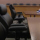 Empty conference room with black leather chairs around a long wooden table; hand sanitizer and tissues on a side table in the background.