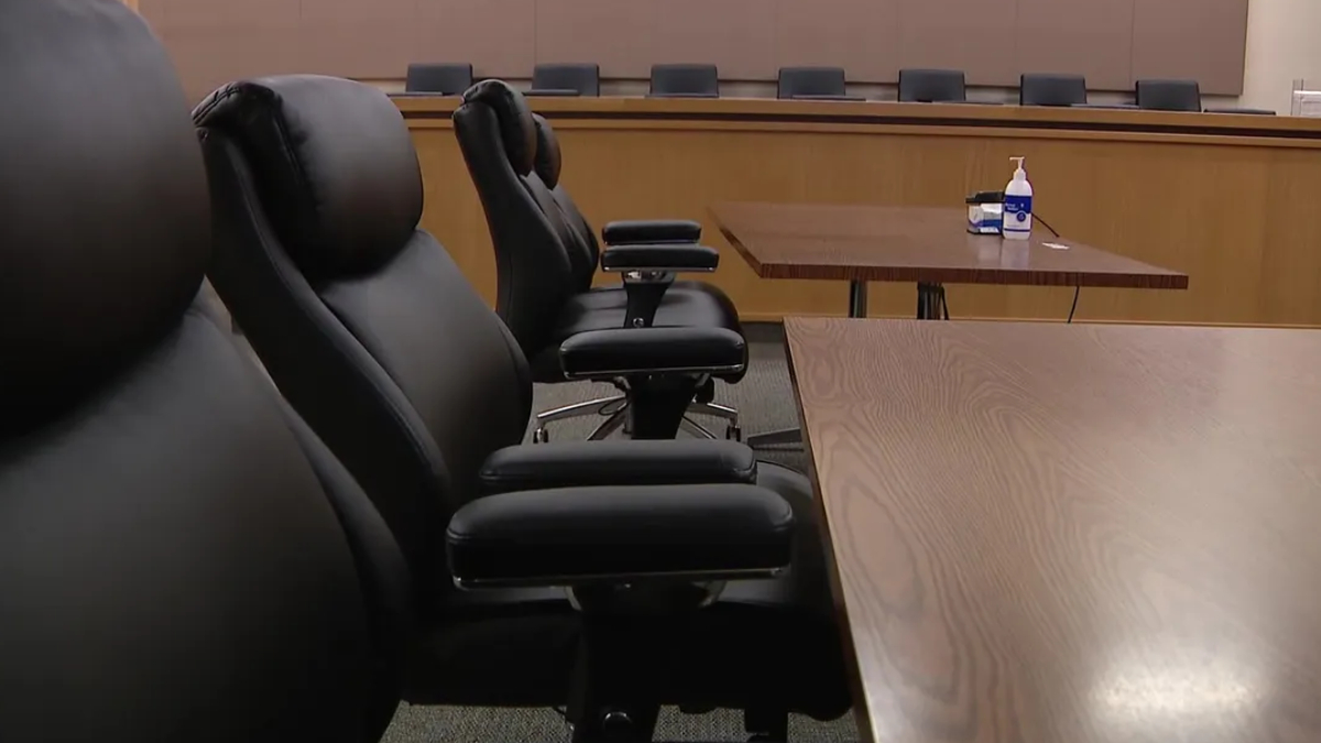 Empty conference room with black leather chairs around a long wooden table; hand sanitizer and tissues on a side table in the background.