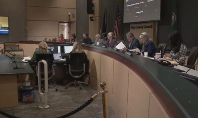 King County Council chamber with officials seated at a curved dais, an American flag, and a large screen in the background.