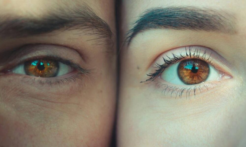 Close-up of two brown eyes side by side, one squinting on the left and the other wide open on the right, showing lashes and skin texture.