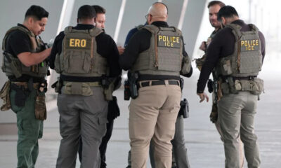 Group of officers in tactical vests labeled POLICE ICE, standing in a circle for briefing.