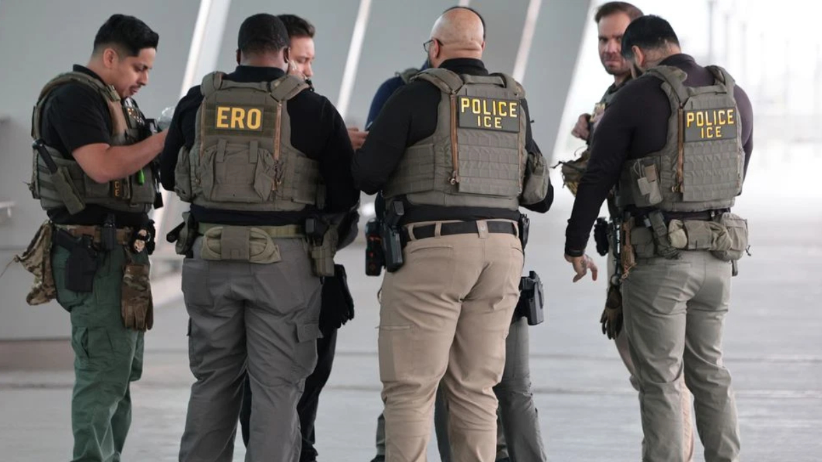 Group of officers in tactical vests labeled POLICE ICE, standing in a circle for briefing.
