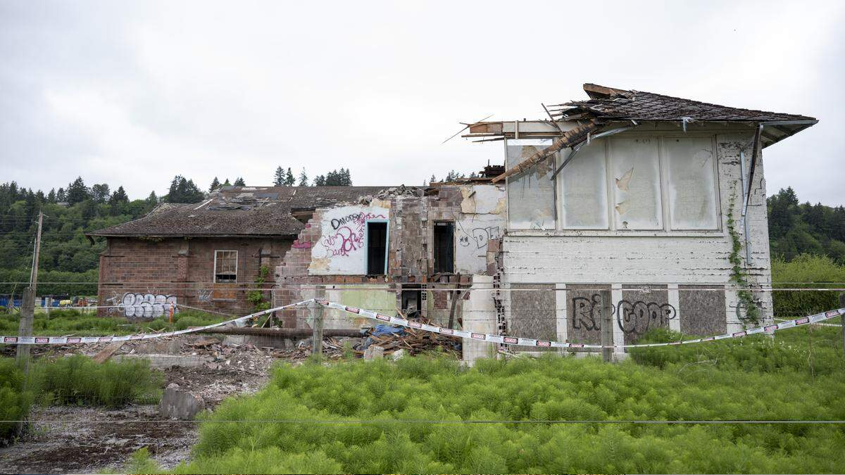Abandoned, partially collapsed brick building with graffiti, surrounded by caution tape in a grassy lot.
