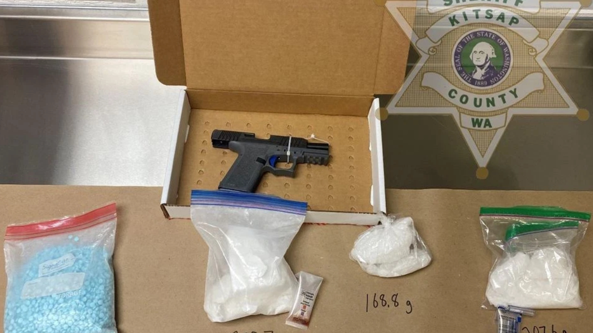 Semi-automatic pistol in an open cardboard evidence box, surrounded by bags of white powder and a small vial, with a handwritten weight (168.9 g) on the table and a sheriff emblem in the background.