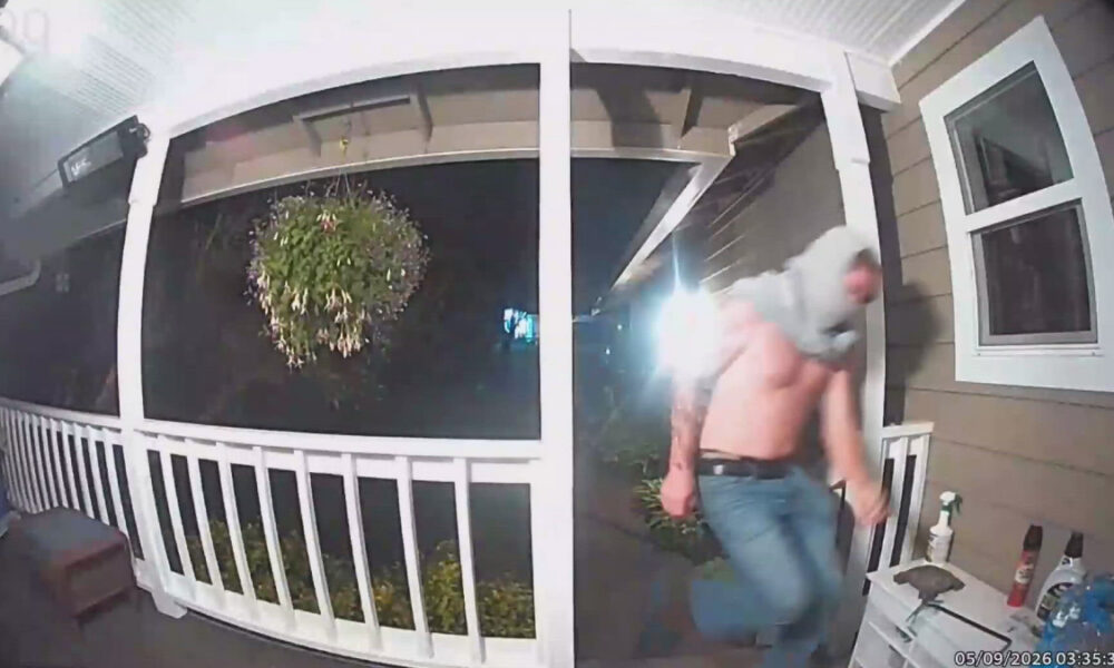 Nighttime porch security footage: a man in jeans and a hoodie runs away from the doorway on a covered porch.
