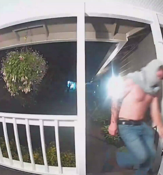Nighttime porch security footage: a man in jeans and a hoodie runs away from the doorway on a covered porch.