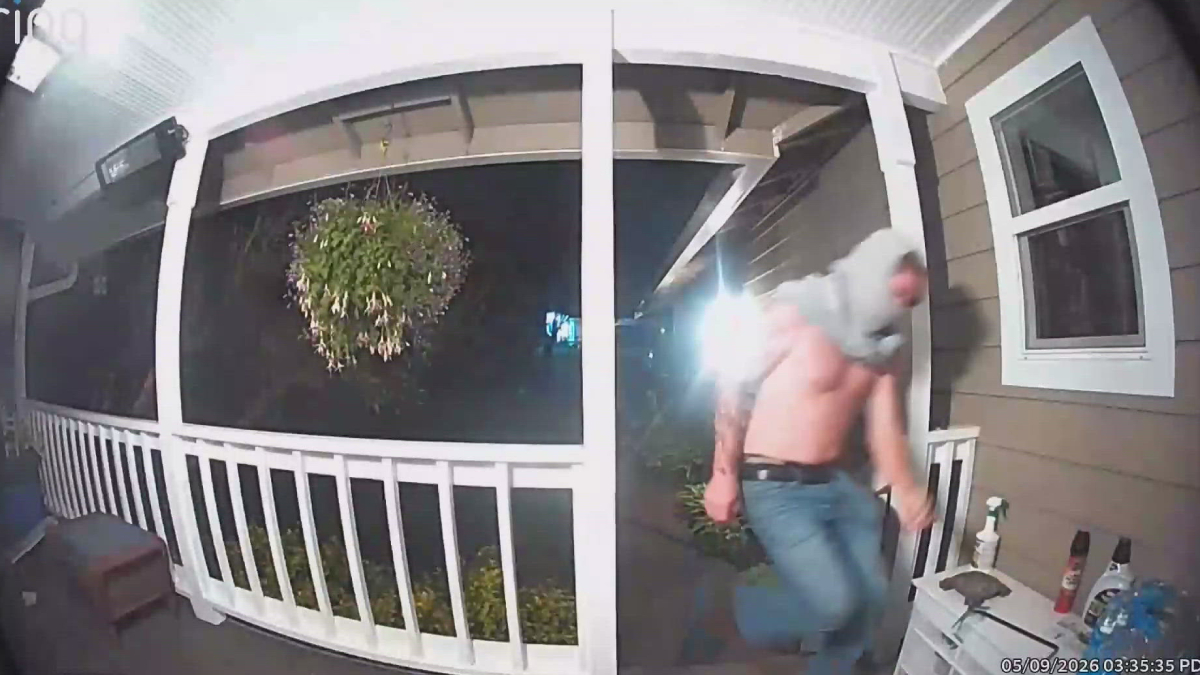 Nighttime porch security footage: a man in jeans and a hoodie runs away from the doorway on a covered porch.