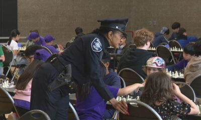 Uniformed police officer bends to help a child during a crowded community chess event in a large hall.