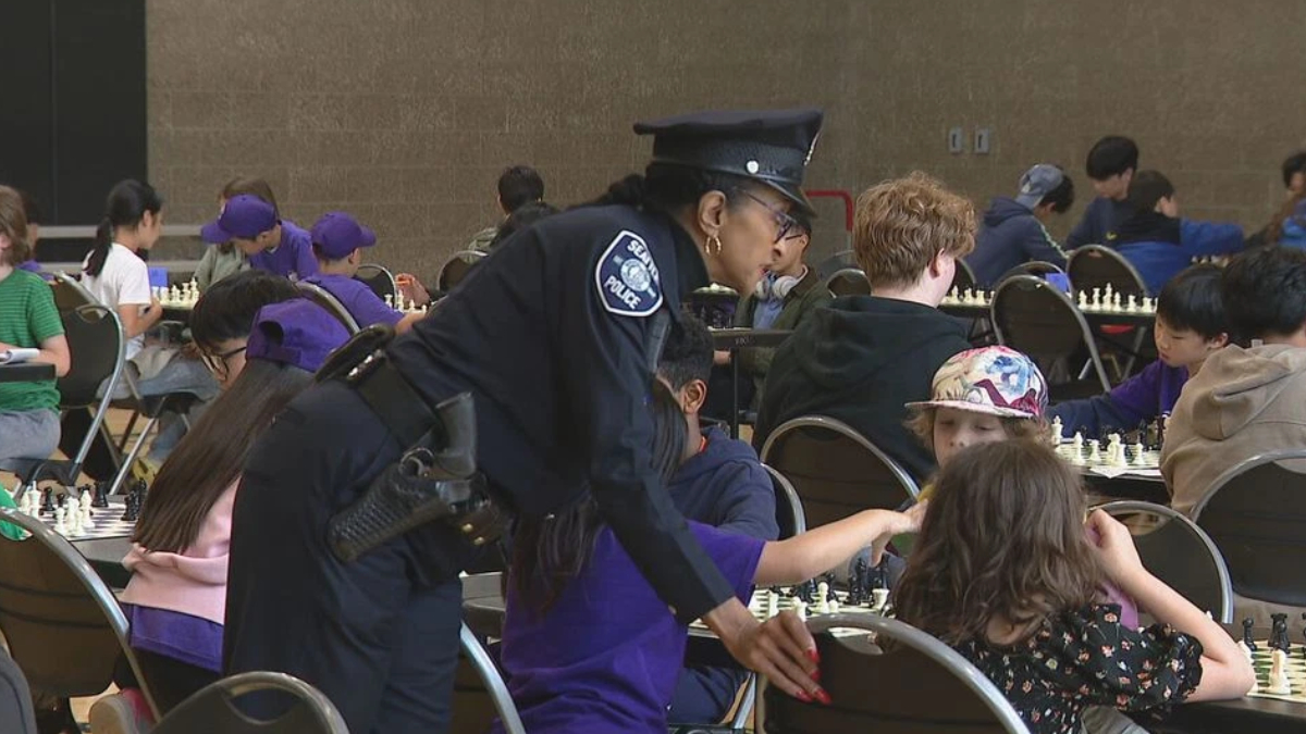 Uniformed police officer bends to help a child during a crowded community chess event in a large hall.