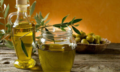 Olive oil bottle and mason jar on a rustic wooden table with olive branches and a bowl of green olives nearby.