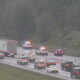 Emergency responders with flashing lights at a multi-vehicle crash on a wet highway, with traffic backed up nearby.