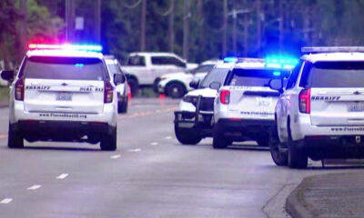 Several police SUVs with red and blue lights flashing on a suburban street, blocking traffic or securing a scene.